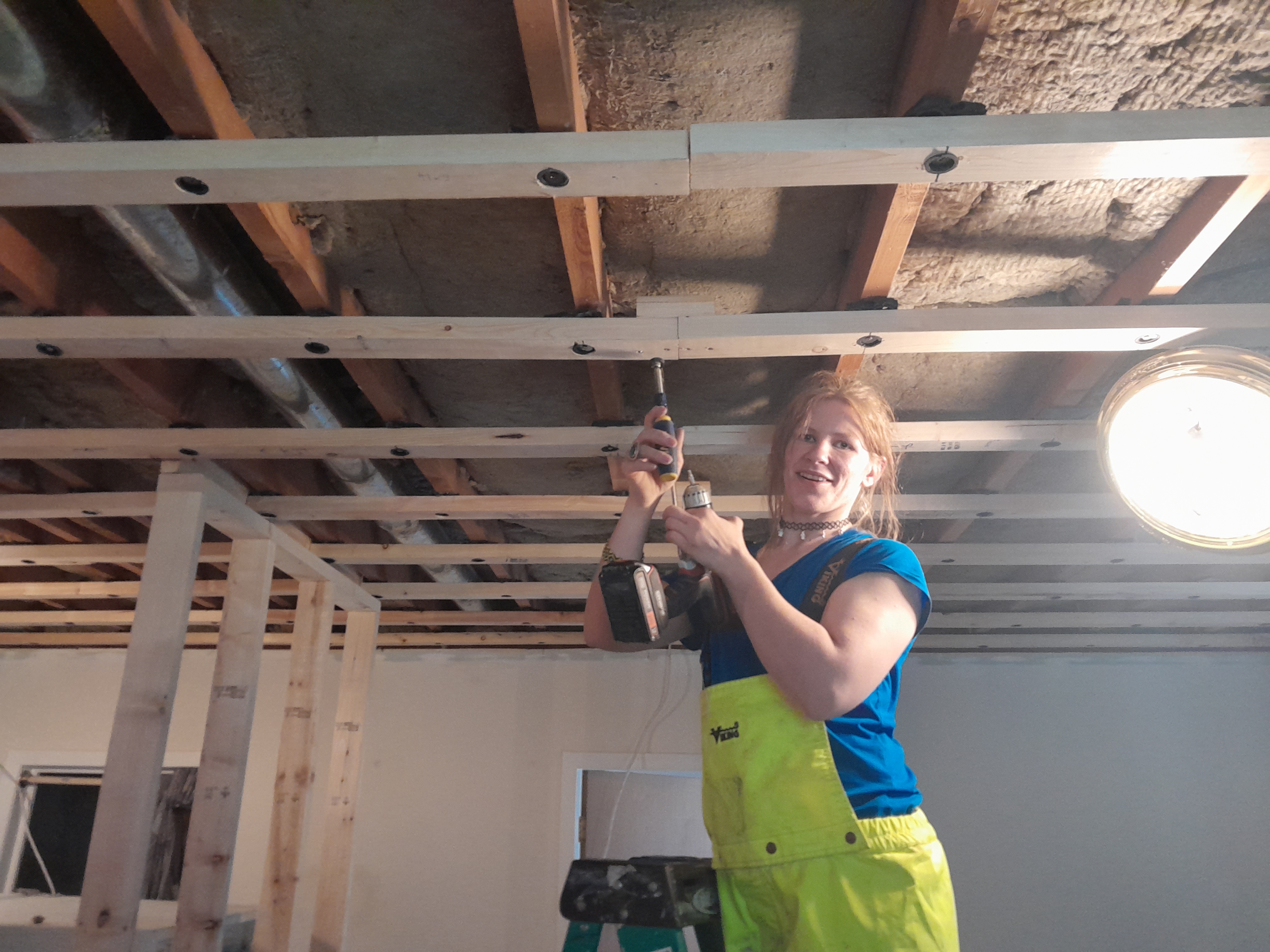 Female renovation worker holding a tool as she works on the basement ceiling
