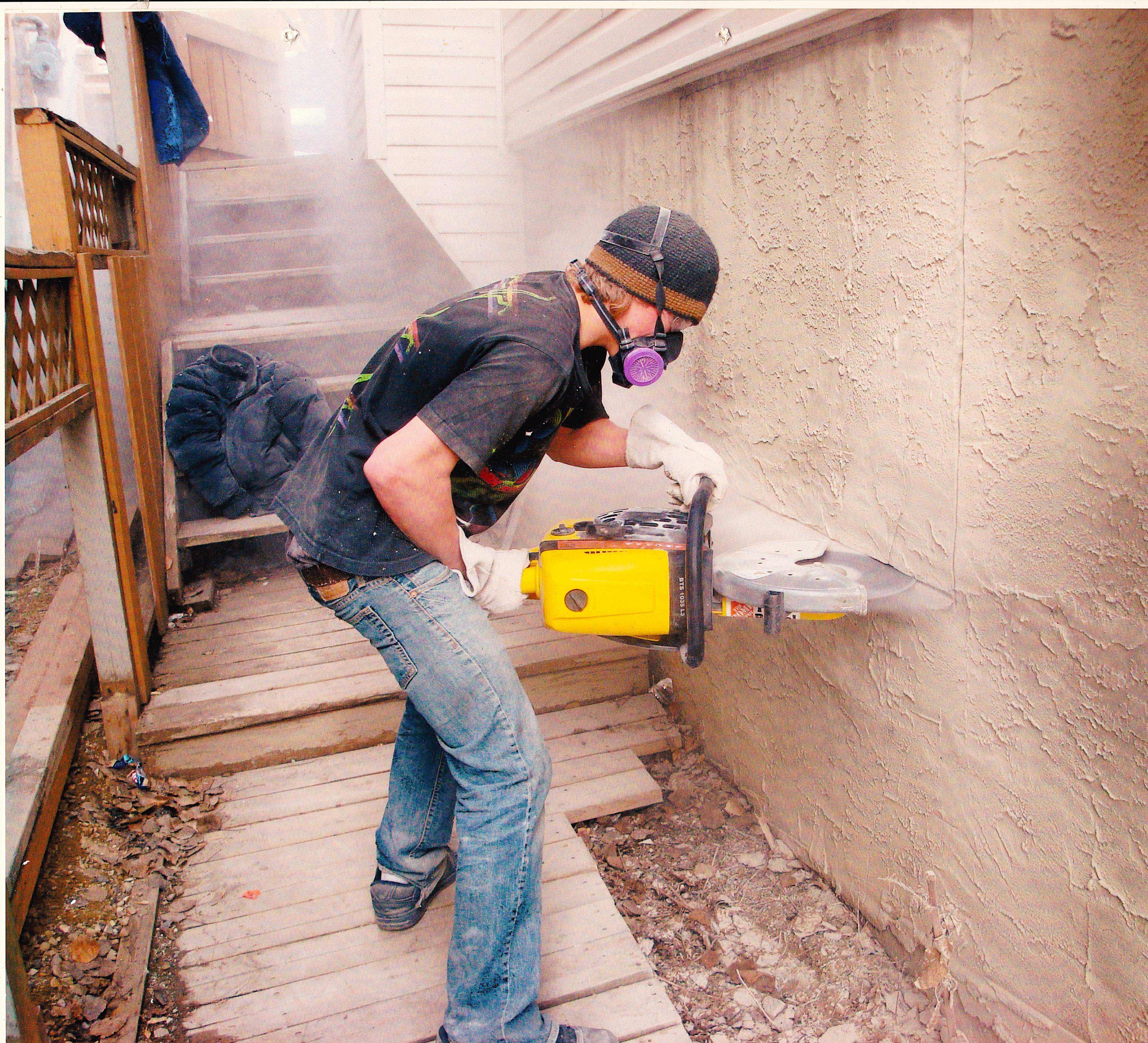 A renovation worker cutting an egress window into a basement from the outside.